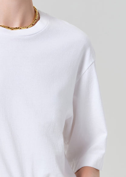 Person wearing a white t-shirt and white shorts with a belt on a plain background