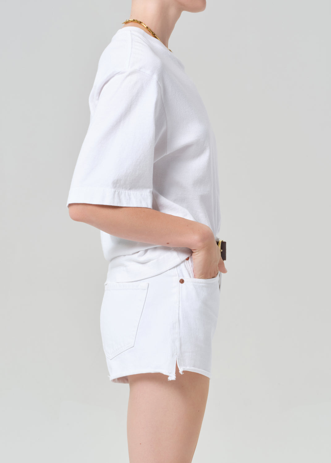 Person wearing a white t-shirt and white shorts with a belt on a plain background