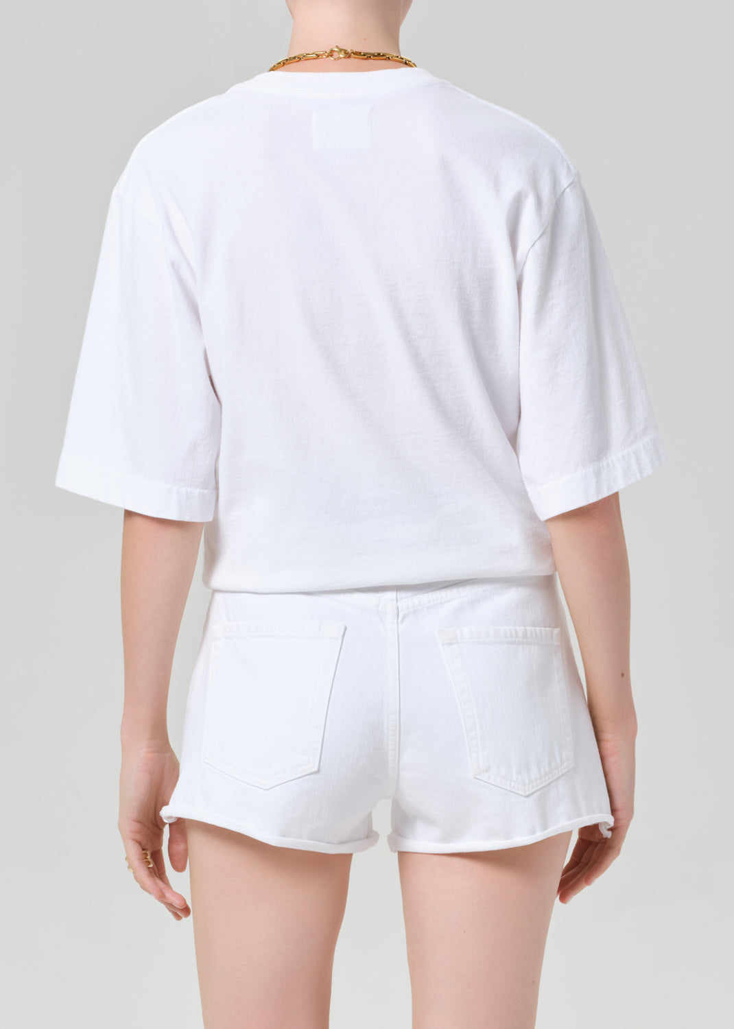 Person wearing a white t-shirt and white shorts with a belt on a plain background