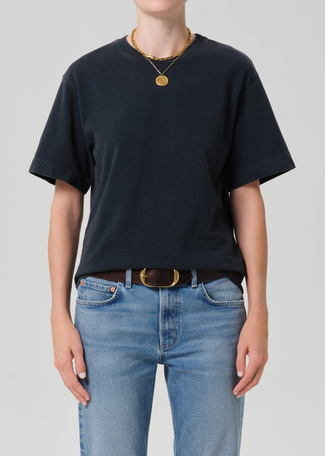 Person wearing a black t-shirt and blue jeans with a plain background