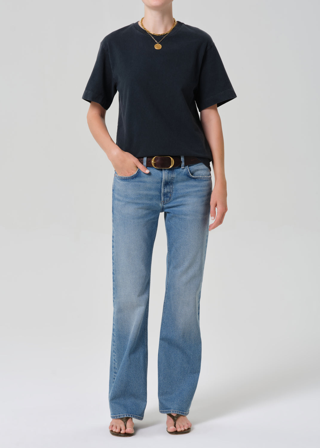 Person wearing a black t-shirt and blue jeans with a plain background