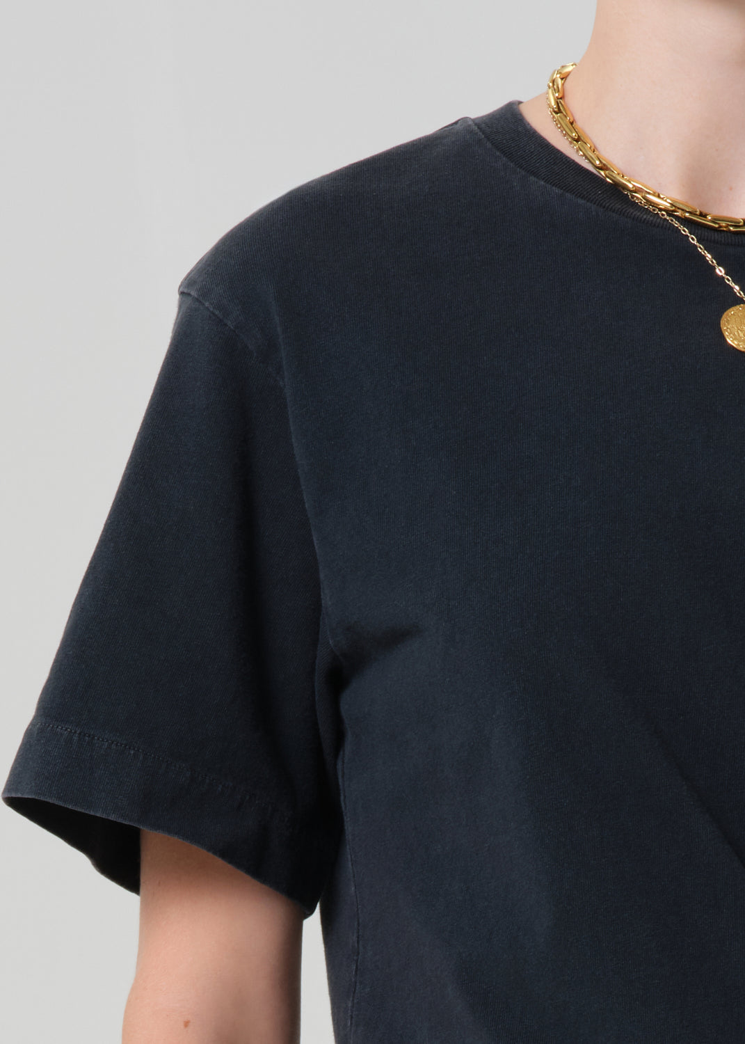 Person wearing a black t-shirt and gold necklace on a plain background