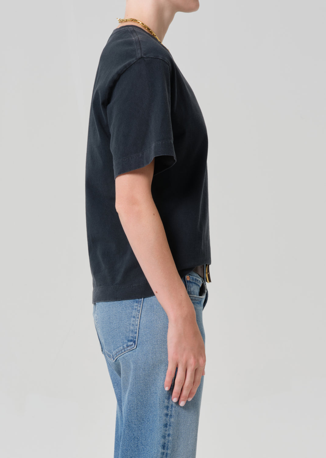 Person wearing a black t-shirt and blue jeans with a plain background