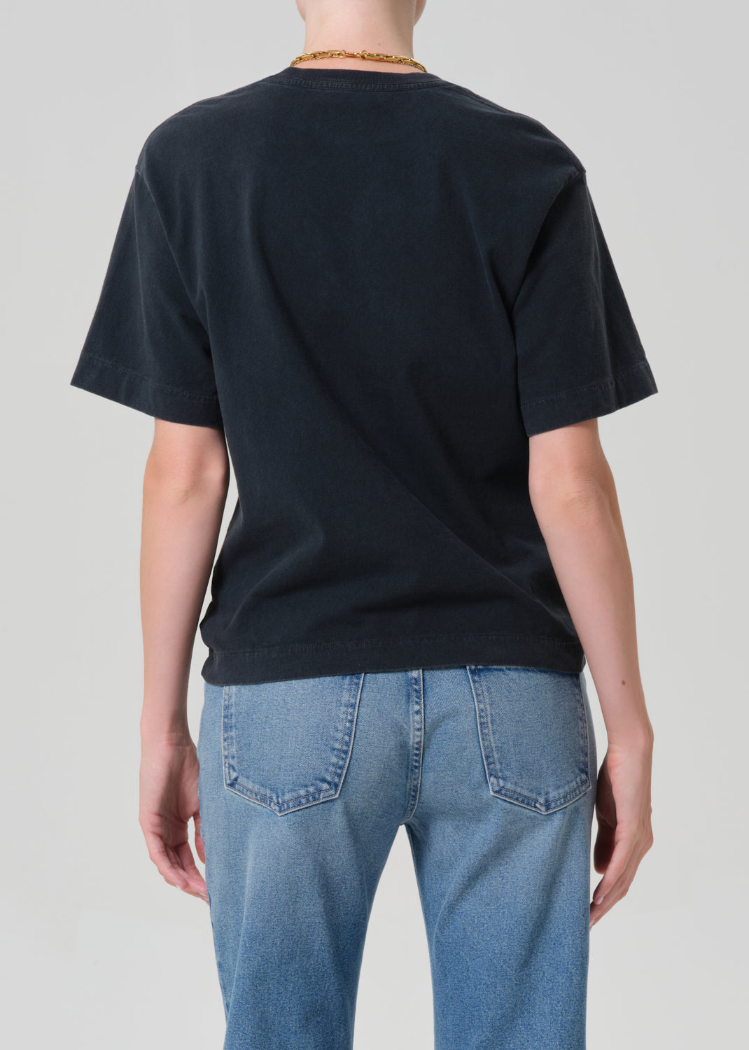 Person wearing a black t-shirt and blue jeans with a plain background