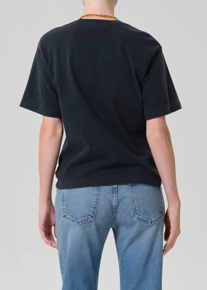 Person wearing a black t-shirt and blue jeans with a plain background