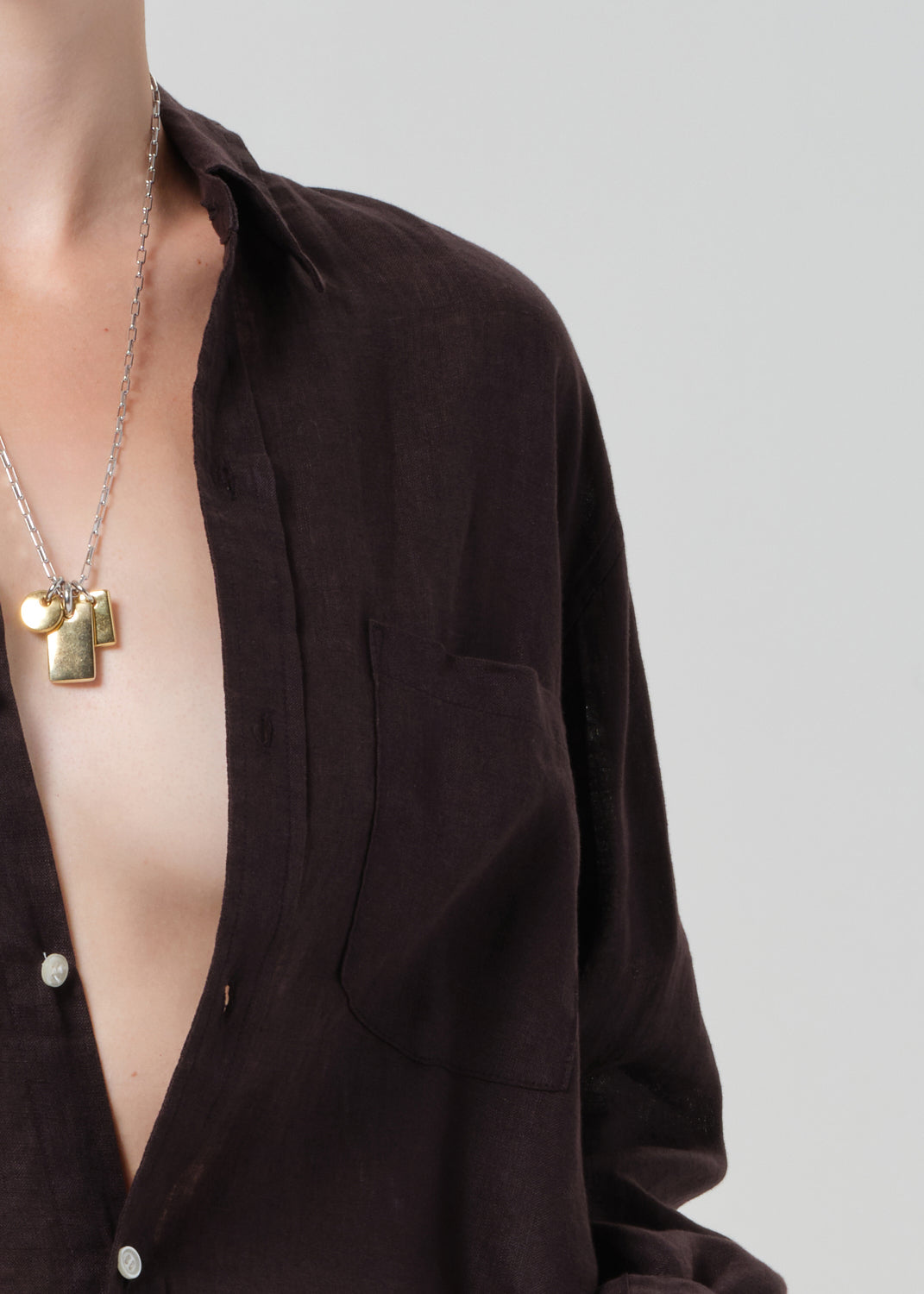 Person wearing a dark brown shirt with a necklace on a light gray background