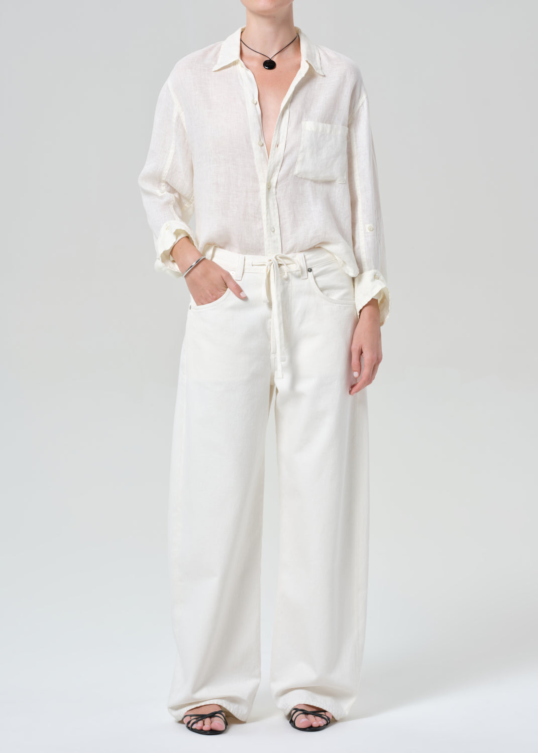 Person wearing a white button-up shirt and wide-leg pants on a plain background