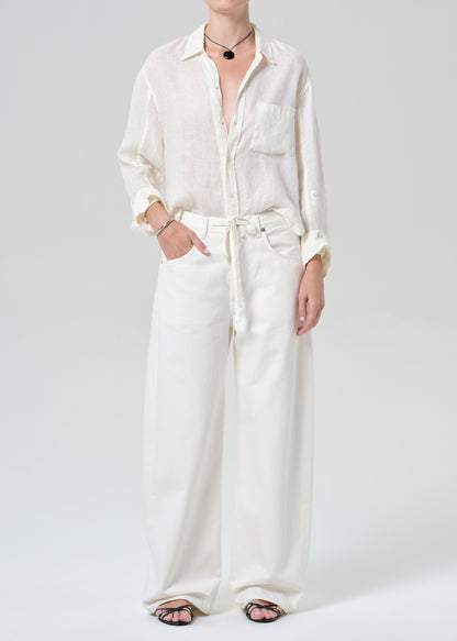 Person wearing a white button-up shirt and wide-leg pants on a plain background