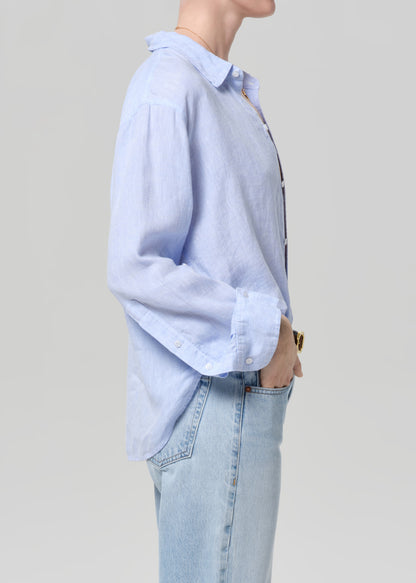 Person wearing a light blue button-up shirt and light blue jeans against a plain background