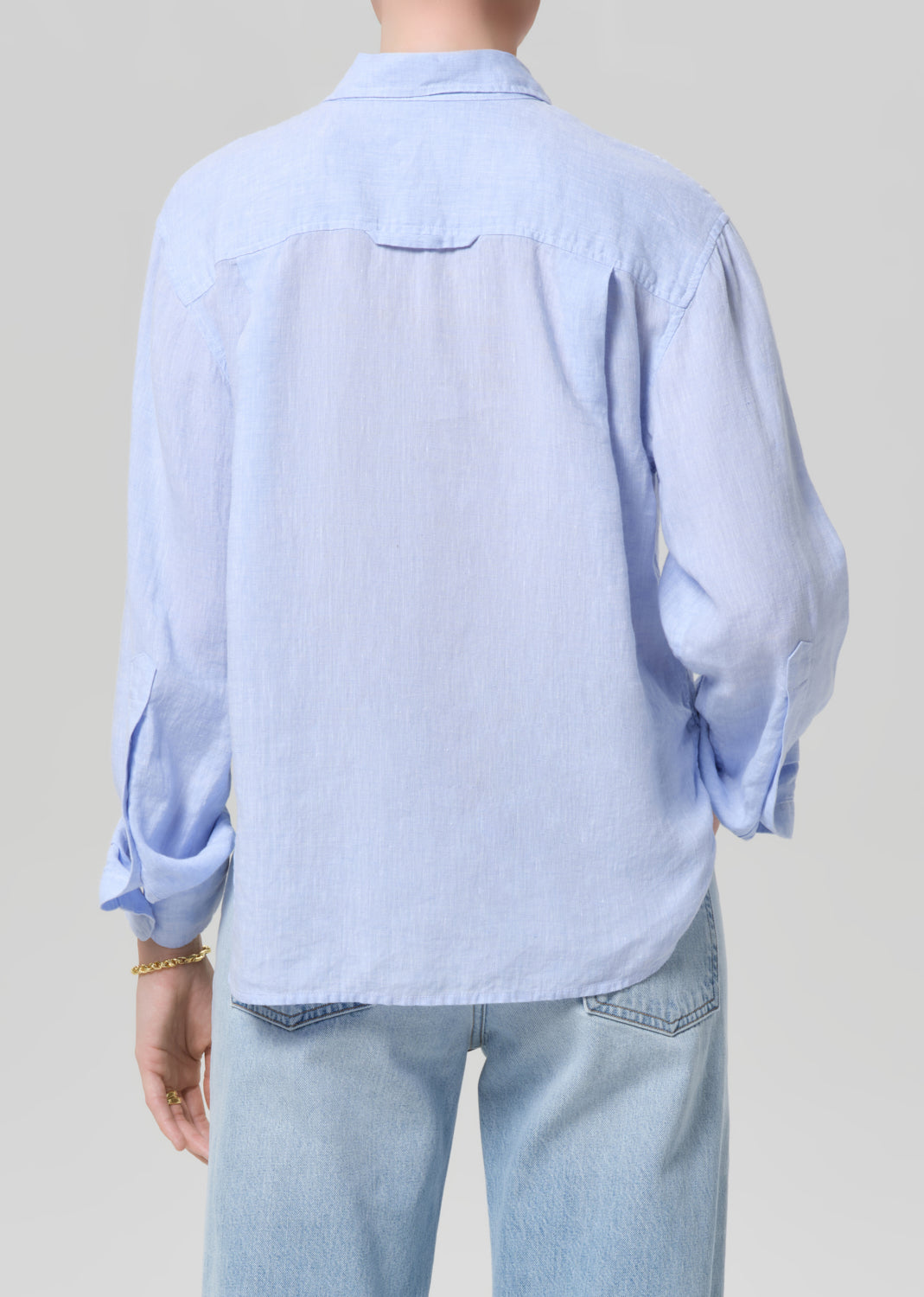 Person wearing a light blue shirt and jeans on a plain background
