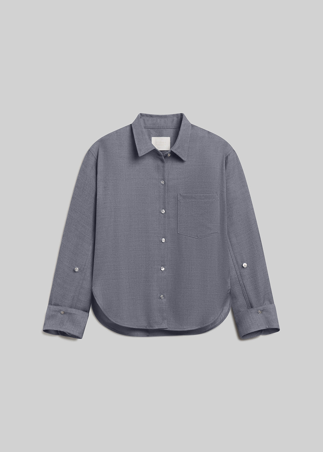 Gris grey long-sleeve wool button-down shirt with a pointed collar, front button closure, single chest pocket, buttoned cuffs, and curved hem, front flat lay view on a grey background.