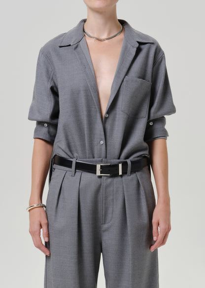 A model wearing a gray two-piece set consisting of a short-sleeve button-up shirt and matching pleated trousers, styled with a black belt and silver hardware.