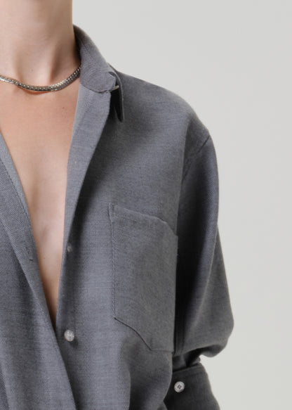 Close-up of a person wearing a gray knit button-front shirt with a collar and chest pocket, paired with a silver chain necklace, against a light gray background.