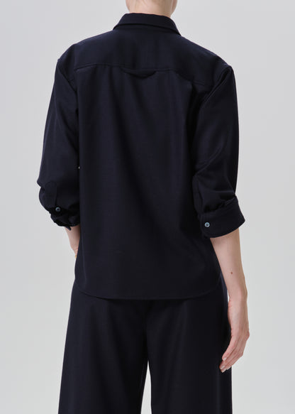 Rear view of a person wearing a dark navy long-sleeve button-up shirt with rolled sleeves and matching dark navy trousers, against a grey background.