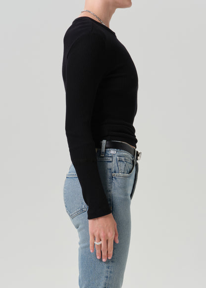 A side-profile view of a person wearing a fitted black long-sleeve ribbed top and light blue jeans against a grey background.