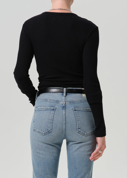 Rear view of a model wearing a black ribbed long-sleeve top and light blue jeans with a black belt, against a grey background.