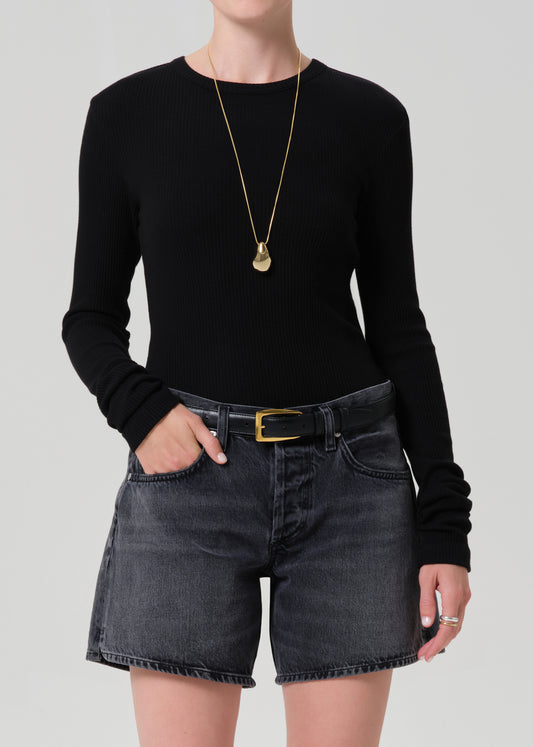 Person wearing a black long-sleeve top and washed black denim shorts on a plain background