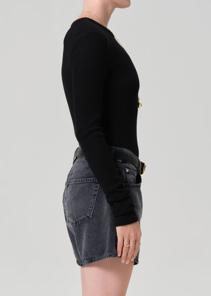 Person wearing a black long-sleeve top and washed black denim shorts on a plain background