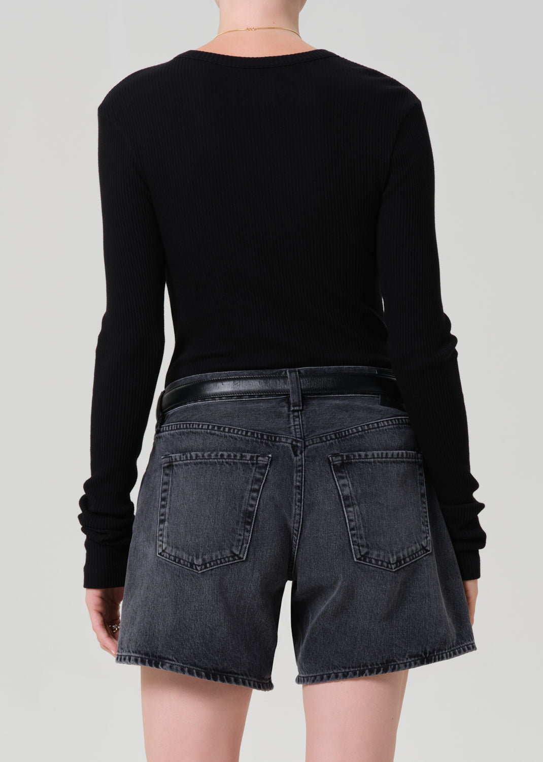 Person wearing a black long-sleeve top and washed black denim shorts on a plain background