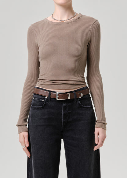 Person wearing a brown ribbed long-sleeve top and black pants on a grey background