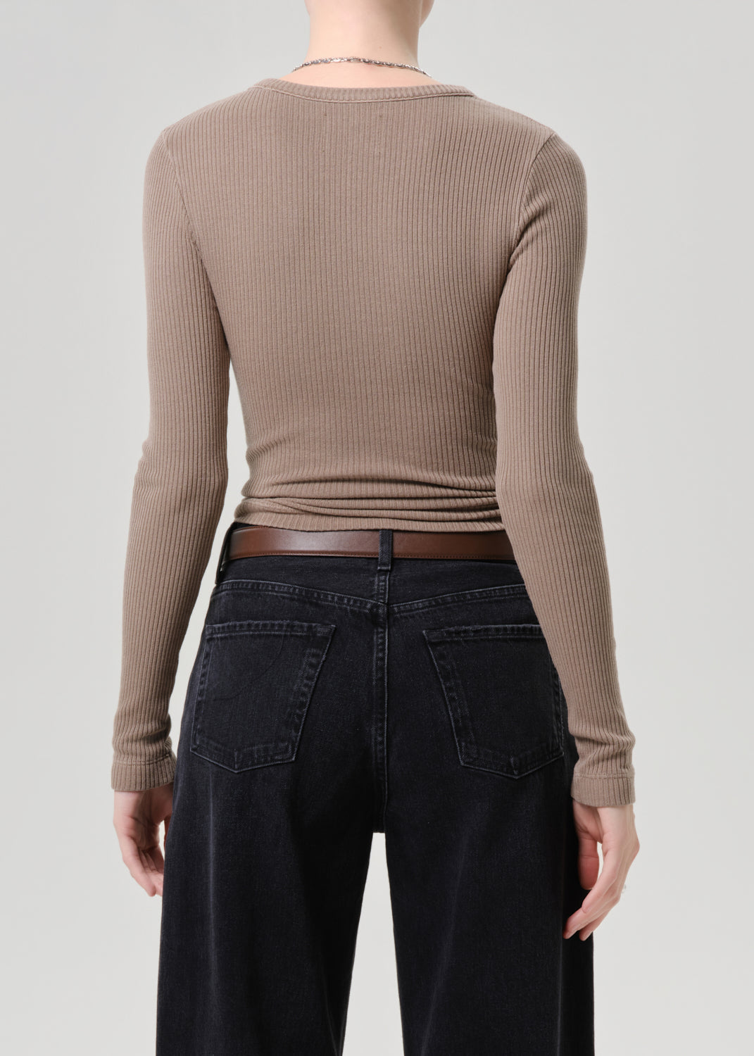 Person wearing a brown ribbed long-sleeve top and black pants on a grey background