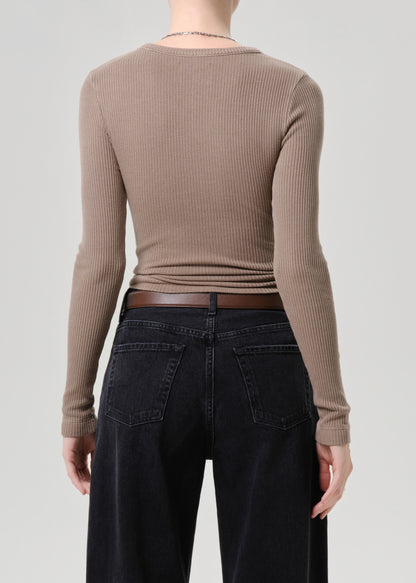 Person wearing a brown ribbed long-sleeve top and black pants on a grey background