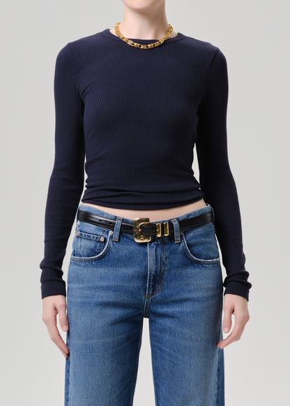 A model wearing a dark navy blue ribbed long-sleeve top tucked into blue jeans with a black belt featuring a gold buckle, accessorized with a gold chain necklace.