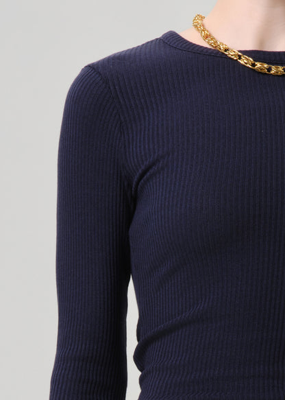 Close-up of a person wearing a dark navy ribbed long-sleeve top with a chunky gold chain necklace, against a grey background.