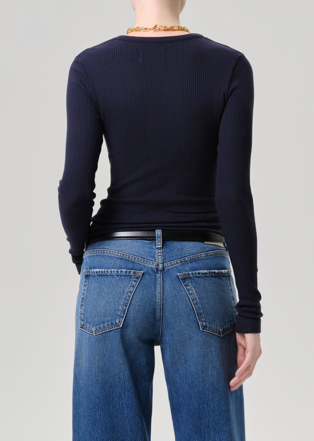 Rear view of a model wearing a dark navy ribbed long-sleeve top and blue jeans against a grey background.