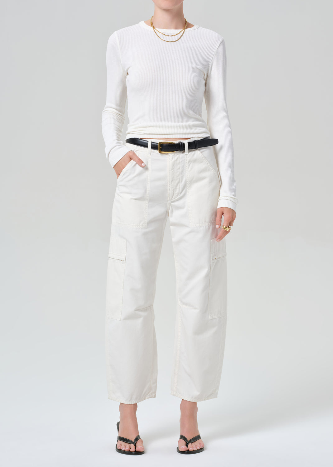 Person wearing a white long-sleeve top and white cargo pants with a black belt on a plain background