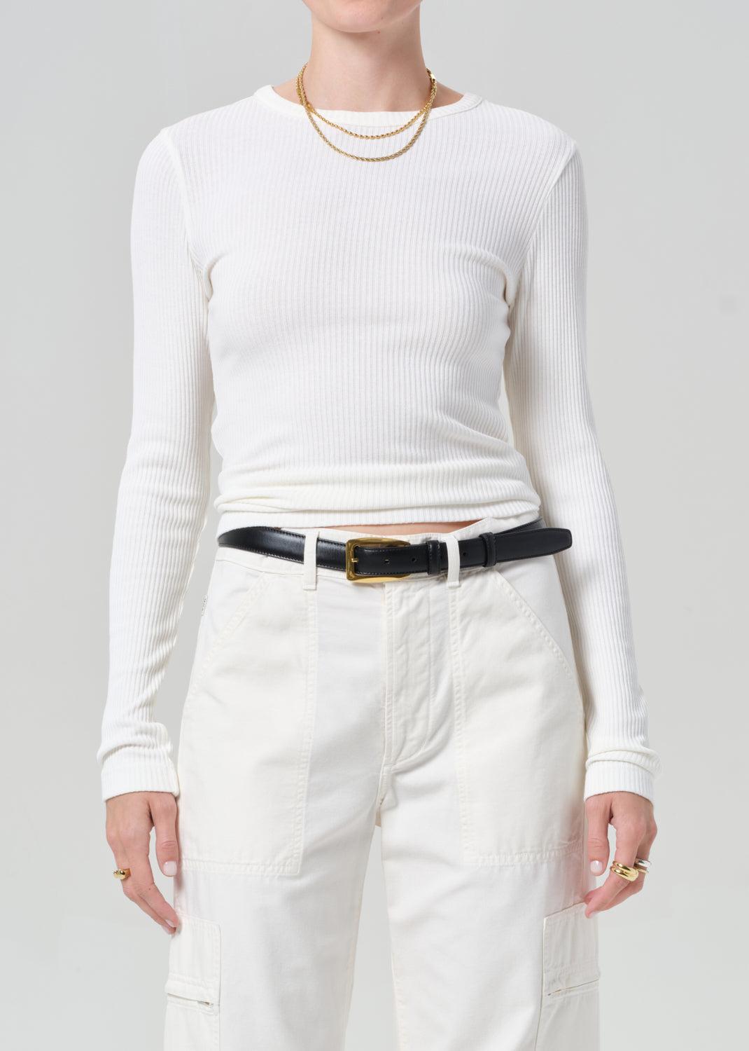 Person wearing a white long-sleeve top and white cargo pants with a black belt on a plain background