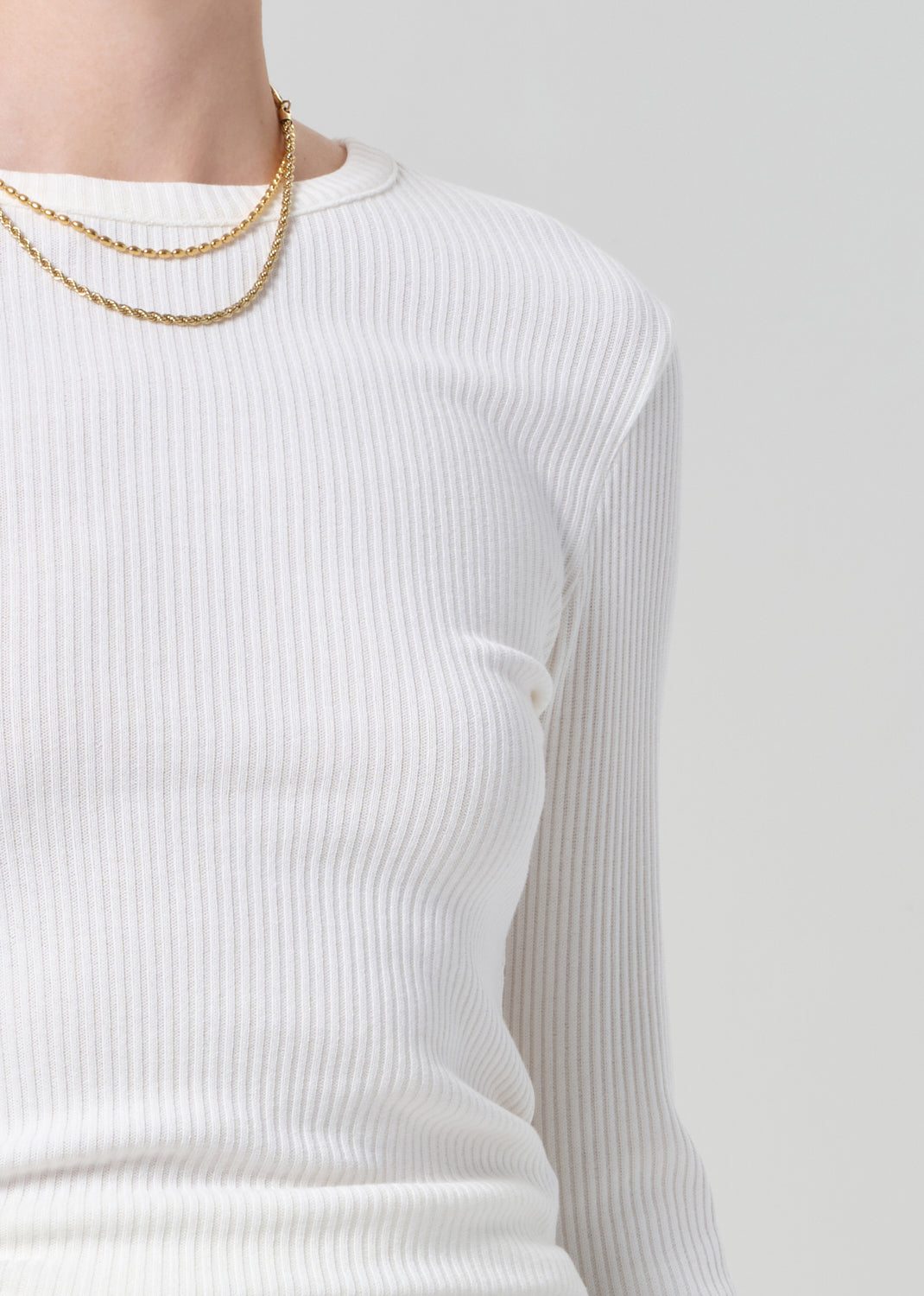 Person wearing a white long-sleeve top on a plain background