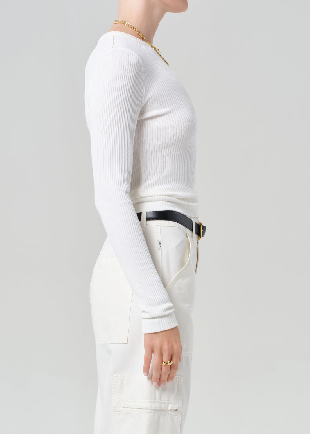 Person wearing a white long-sleeve top and white cargo pants with a black belt on a plain background