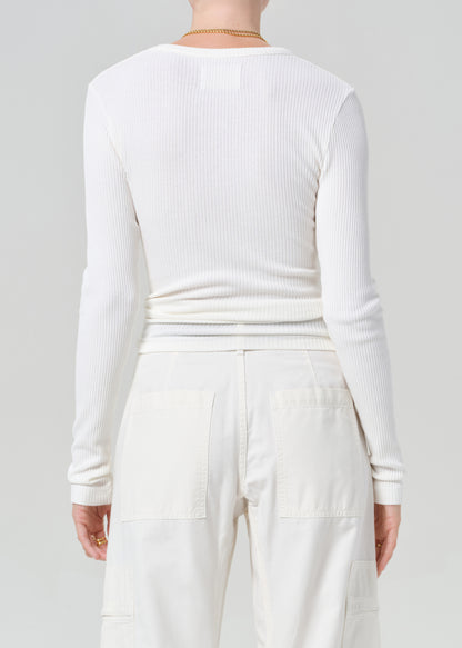 Person wearing a white long-sleeve top and white cargo pants with a black belt on a plain background