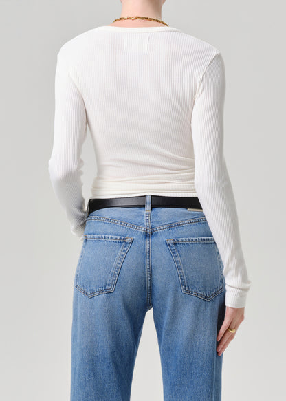 A person shown from the back wearing a fitted white ribbed long-sleeve top, blue jeans, and a black belt against a grey background.