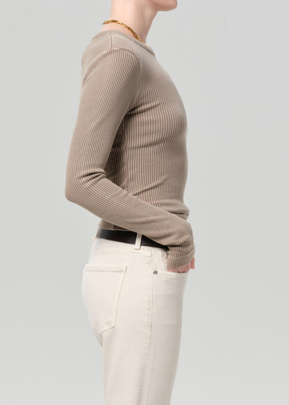 Person wearing a beige ribbed sweater and white pants on a light gray background