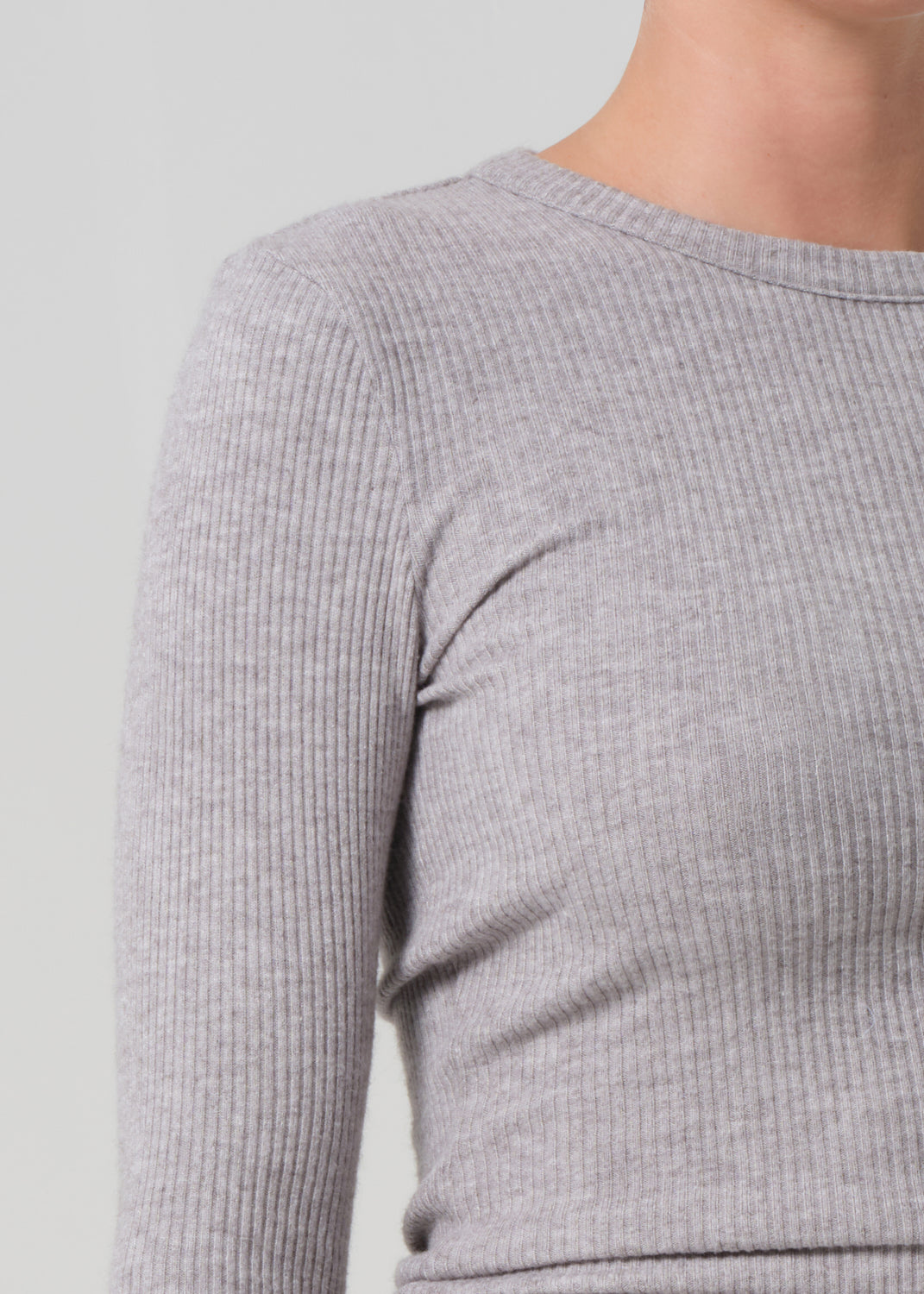Close-up of a person wearing a gray ribbed sweater against a light gray background