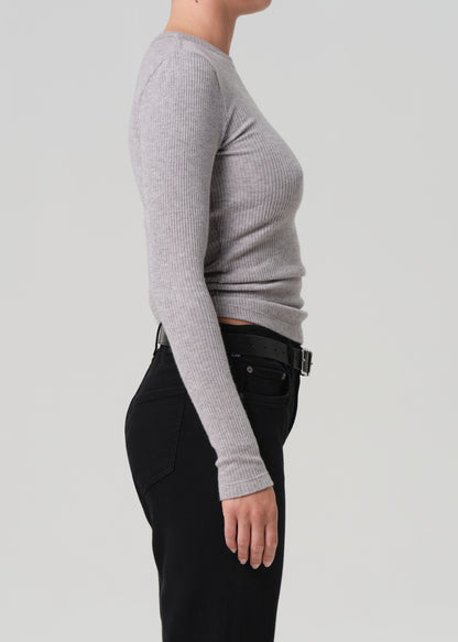 Person wearing a gray long-sleeve top and black pants on a light gray background