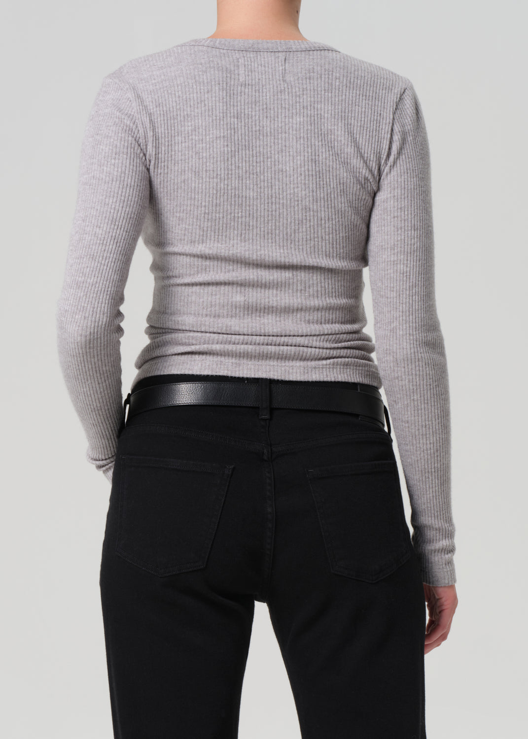Person wearing a gray sweater and black pants on a light gray background