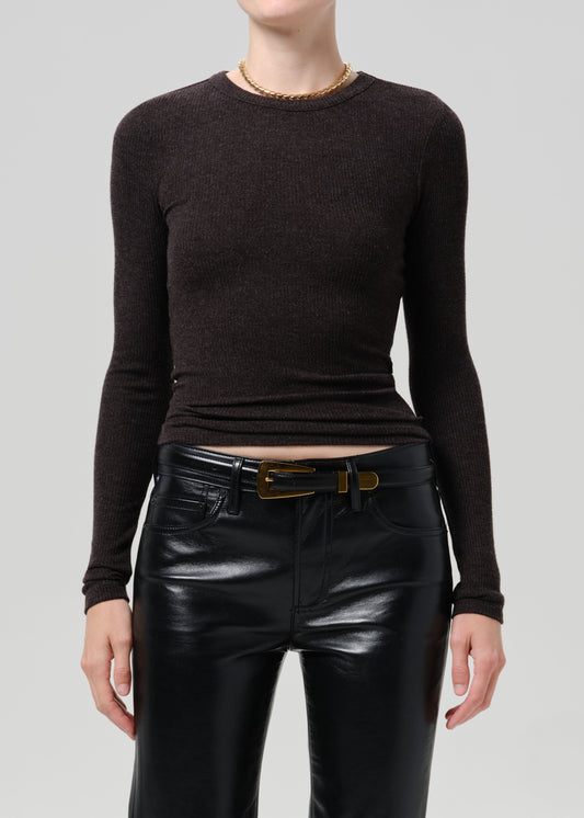 A model wearing a dark brown long-sleeve knit top tucked into black leather pants with a gold belt, shown from the neck down against a grey background.