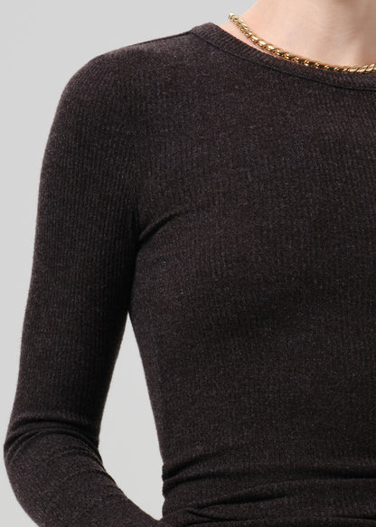Close-up of a person wearing a dark brown ribbed knit long-sleeve top with a gold chain necklace, against a light grey background.