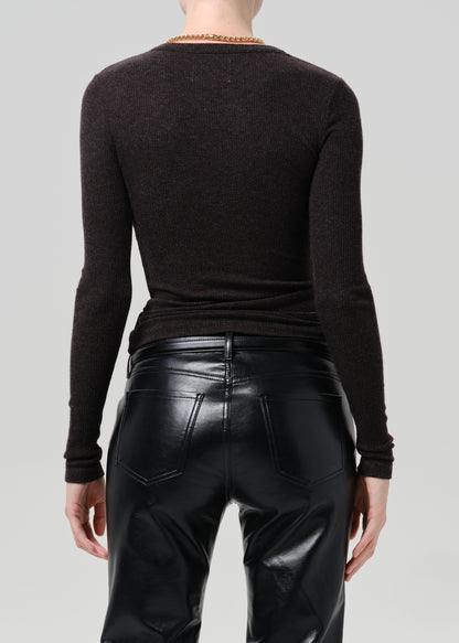 Rear view of a model wearing a dark brown long-sleeve knit top and black faux-leather pants against a grey background.