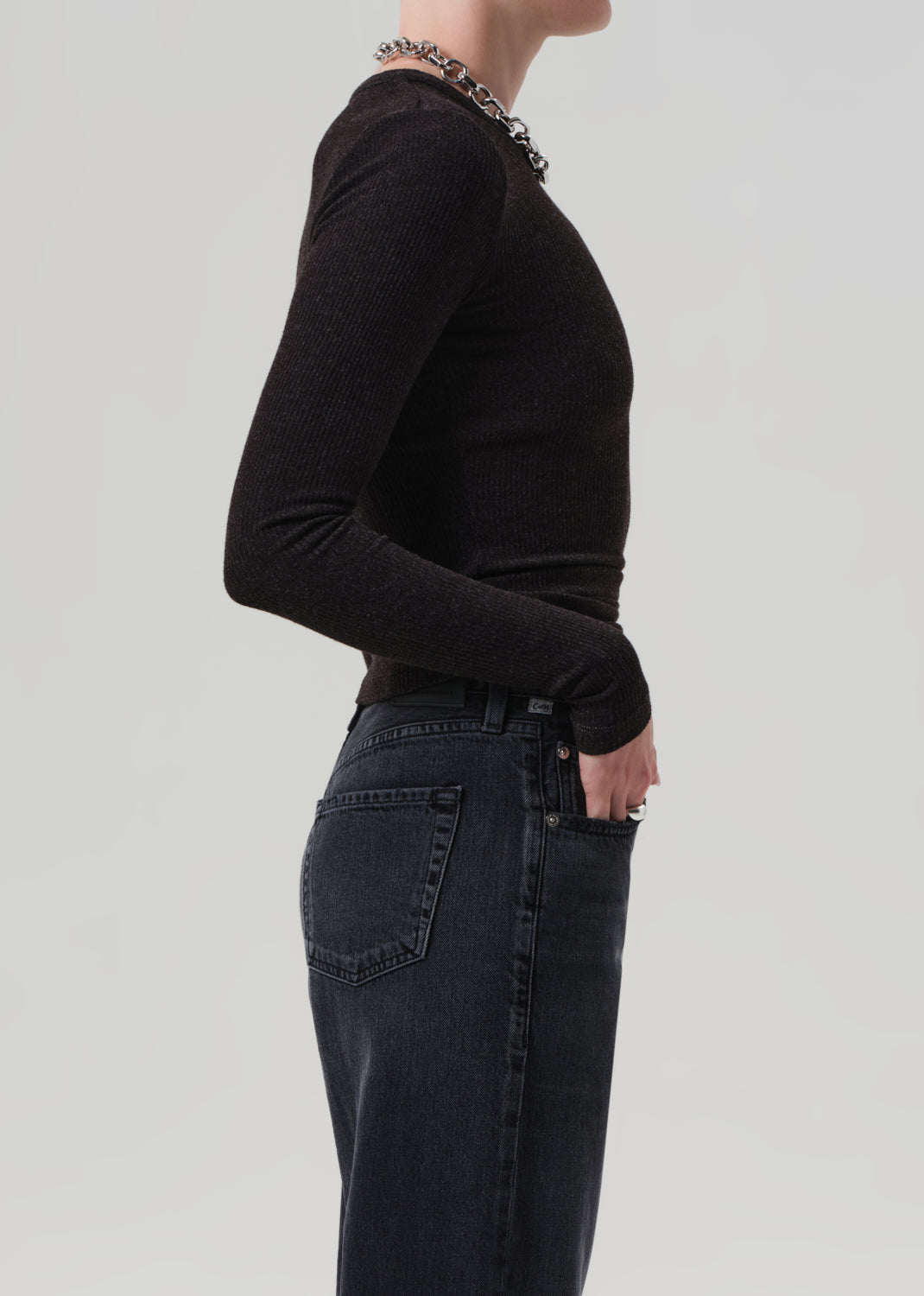 Person wearing a brown long-sleeve top and dark jeans on a light gray background