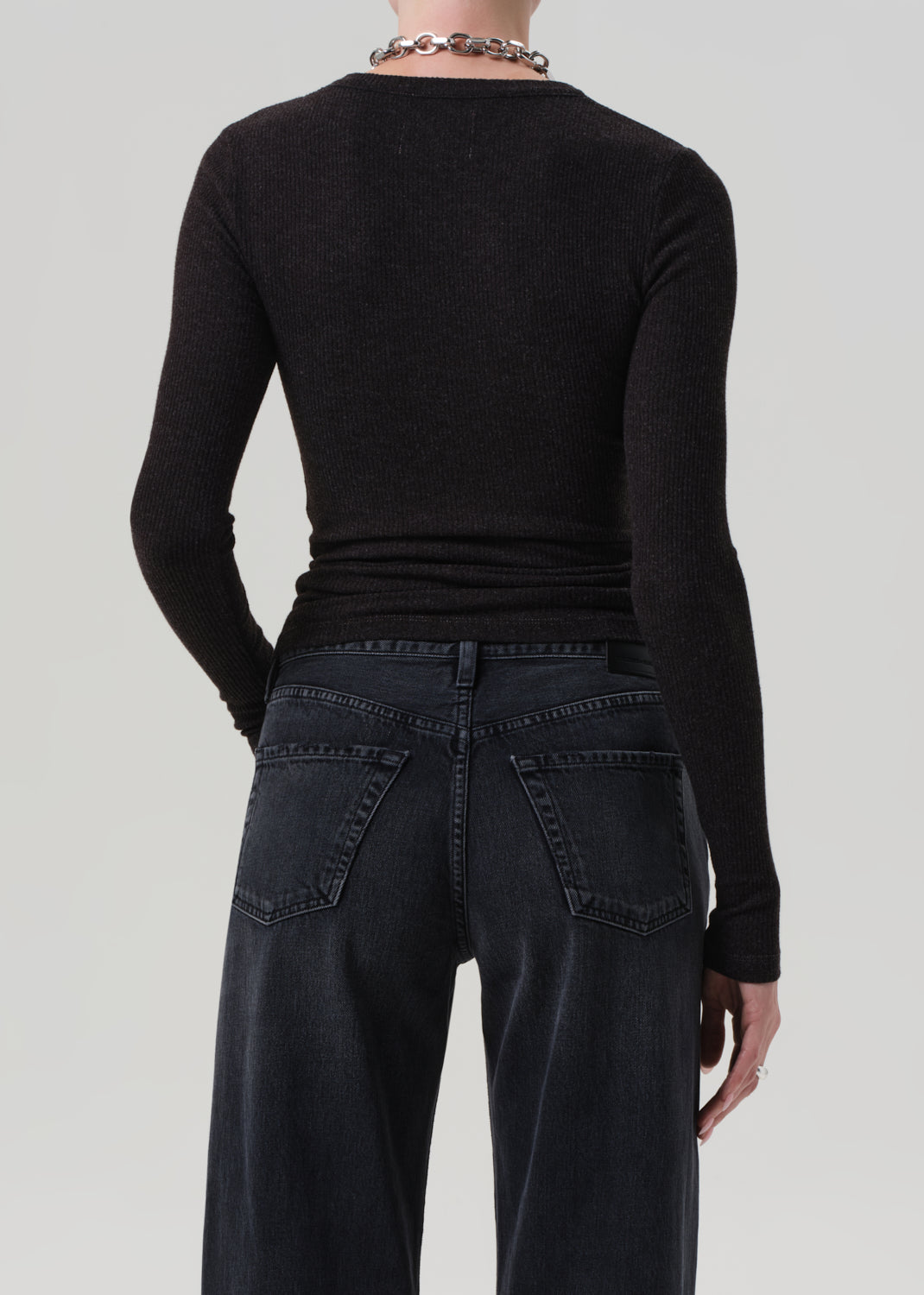 Person wearing a brown long-sleeve top and dark jeans on a light gray background