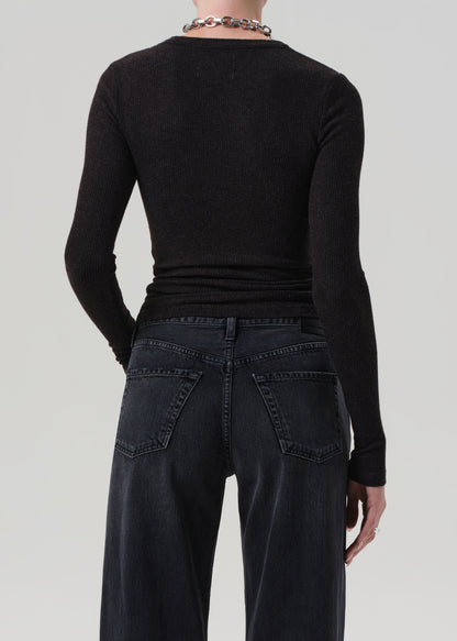 Person wearing a brown long-sleeve top and dark jeans on a light gray background