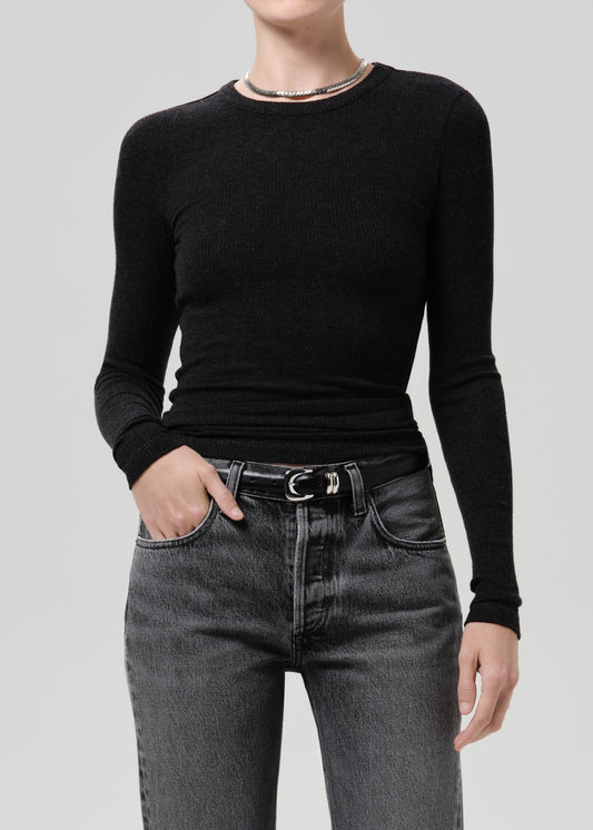 A model wearing a black long-sleeve crewneck ribbed knit top tucked into dark grey jeans with a black belt.