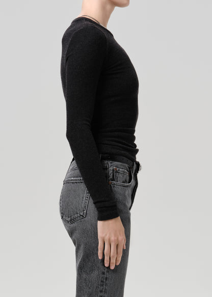 Side profile of a model wearing a black long-sleeve crewneck knit top and dark grey jeans against a grey background.