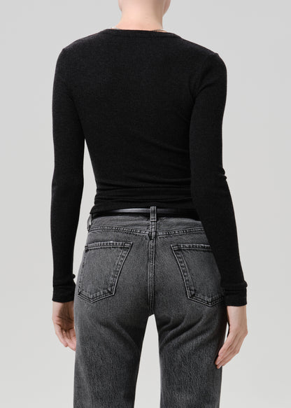 Rear view of a model wearing a black long-sleeve crewneck top tucked into dark grey washed jeans against a grey background.
