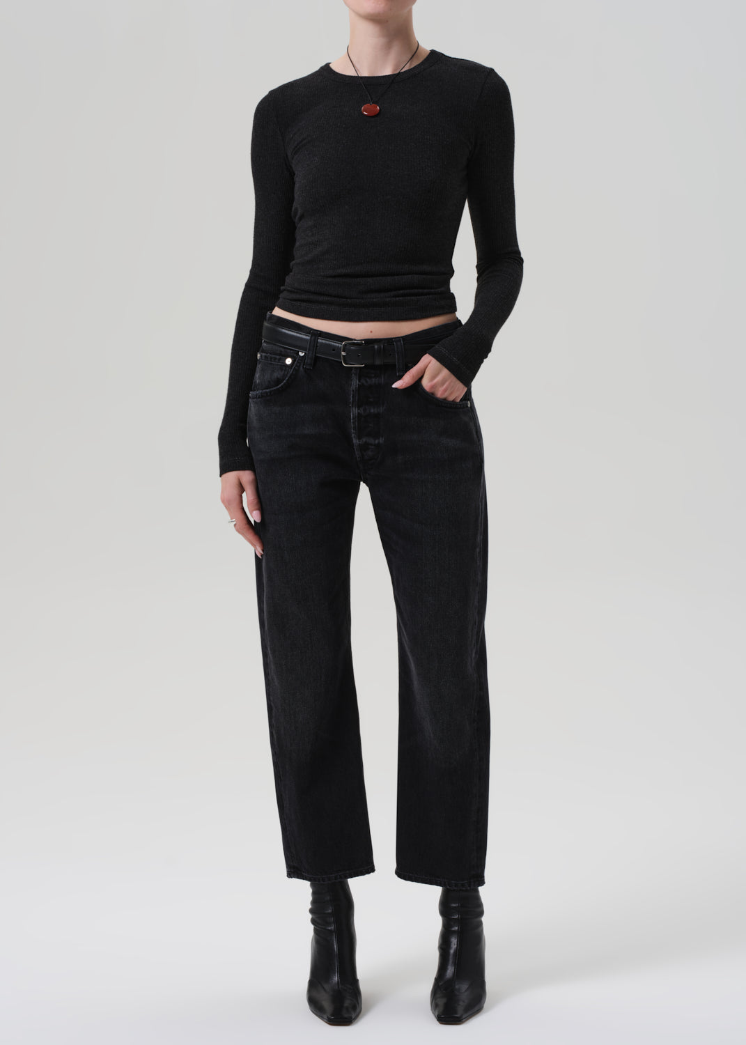 Person wearing a charcoal long-sleeve top and black pants on a light gray background