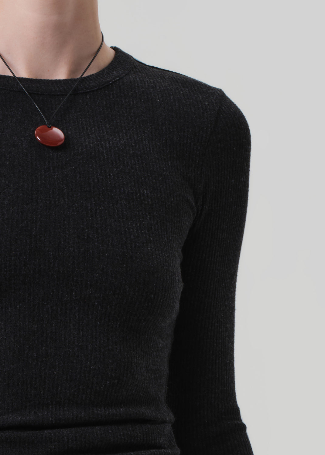 Person wearing a charcoal long-sleeve top and black pants on a light gray background